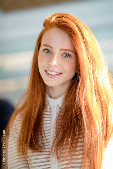 portrait of good looking ginger female with long straight shiny hair and natural make up smiling