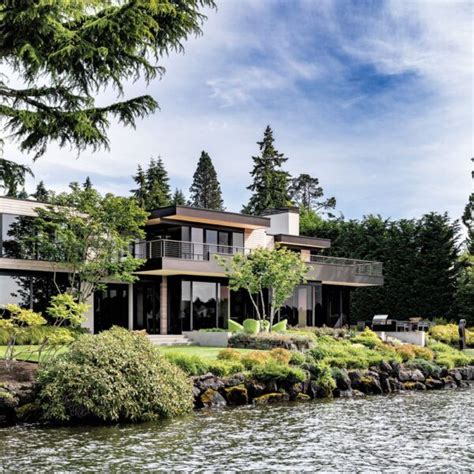 A Large House Sitting On Top Of A Lush Green Hillside Next To A Lake