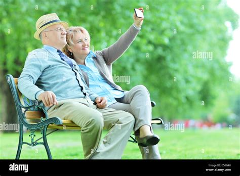 Elderly Couple Taking A Selfie In The Park Seated On Bench Stock Photo