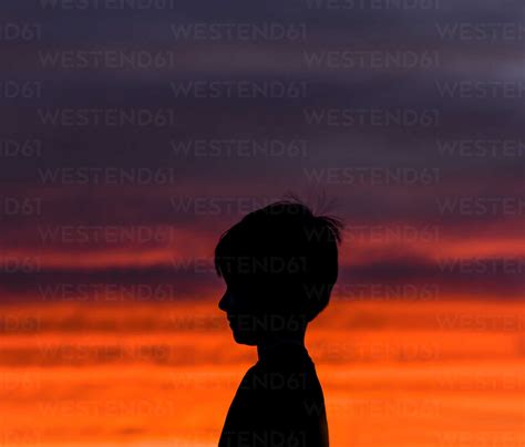 Side View Of Silhouette Boy Standing Against Dramatic Sky In Sunset