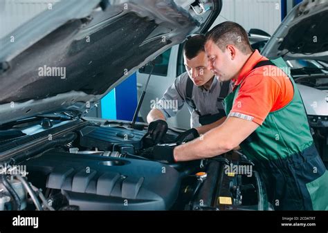 Two Handsome Mechanics In Uniform Are Working In Auto Service Car