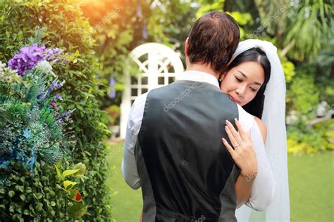 joven asiático novia en blanco vestido de novia es abrazar su marido caucásico novio con amor