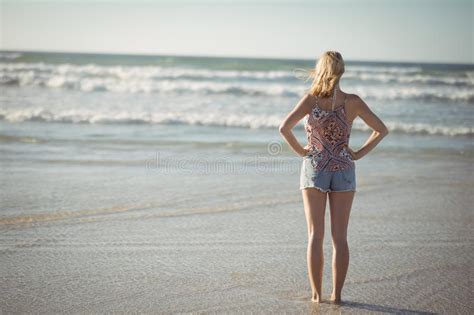 Rear View Of Woman Standing With Hands On Hip At Beach Stock Photo