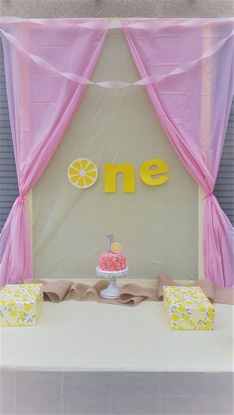 A Table Topped With A Cake Covered In Pink And Yellow Icing Next To A Wall