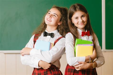 Zwei Lustige Schulmädchen In Den Schuluniformen Sitzen Auf Dem Hintergrund Eines Grünen Brettes