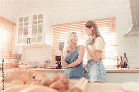 Happy Lesbian Couple Holding Cups Of Coffee In Kitchen Couple Of Lesbian Girls Enjoy Coffee At
