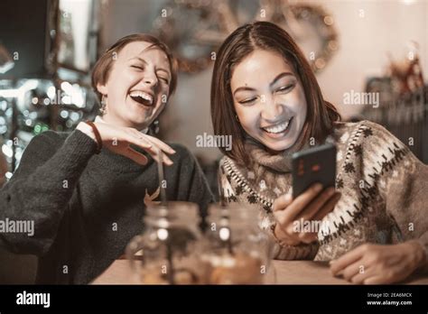 Two Funny Female Friends Look At New Memes On Social Networks And Laugh Out Loud In Cafe