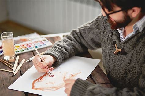 A Man Sitting At A Table Drawing With Colored Pencils And Watercolors