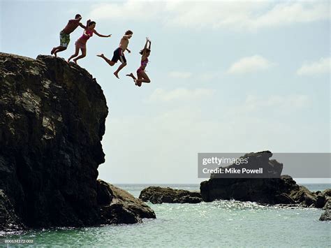 Group Of Friends Jumping Into Ocean From Rock Cliff High Res Stock