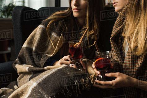 Cropped Image Of Girls Holding Glasses Of Mulled Wine And Sitting