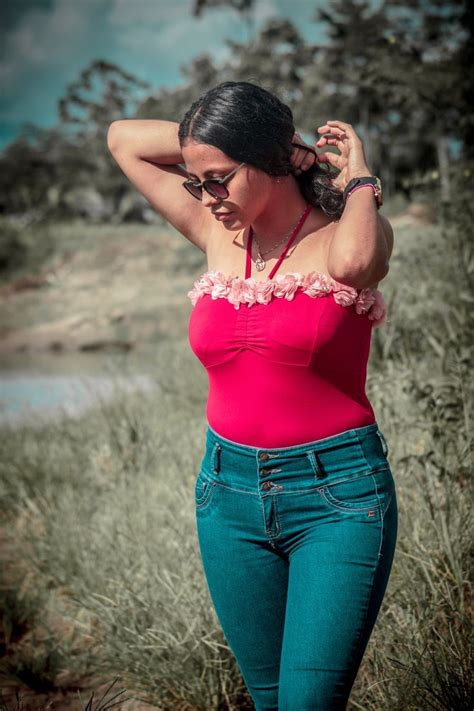 a woman in blue jeans and a pink top is posing for the camera with her hand on her head