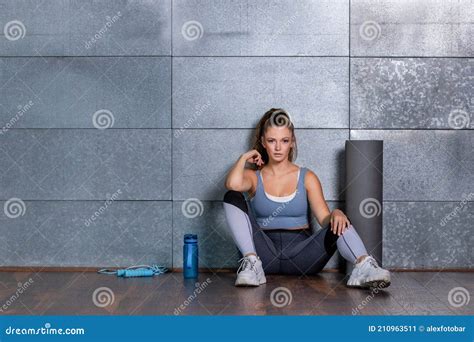 fitness woman sitting on the floor arms rest on her spread legs looking to one site with