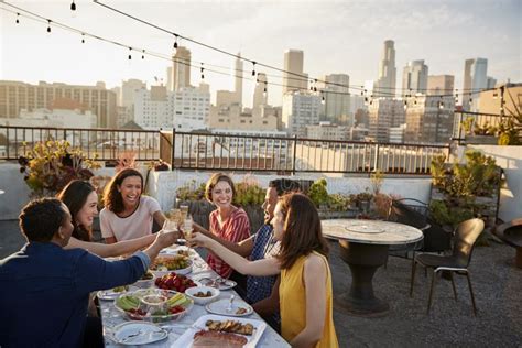 Friends Gathered On Rooftop Terrace For Meal With City Skyline In