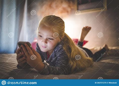 Beautiful Blonde Haired Girl Laying On Her Bed Watching Videos On A Smartphone Stock Image