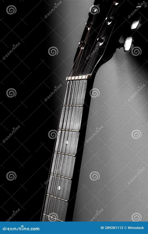 Grayscale Of An Acoustic Guitar Rests Against A Solid Black Wall Stock