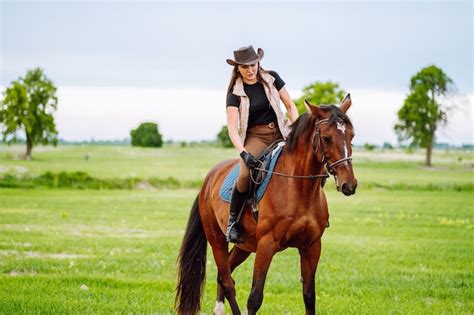 Jovem Mulher Vestida Com Roupas De Montaria E Chapéu Cavalgando Cavalo Marrom Em Campo Verde