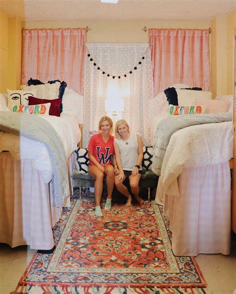 Two Women Sitting On The Floor Next To Twin Beds In A Room With Pink Curtains