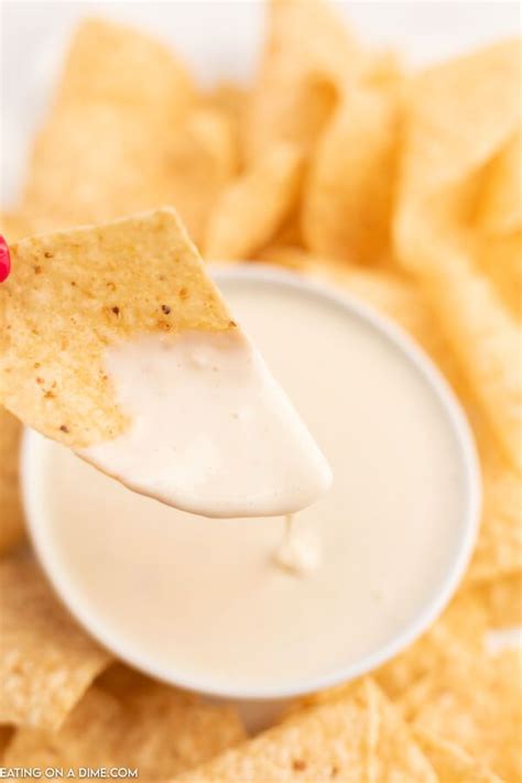 A Person Holding A Tortilla Chip Over A Bowl Of Chips With Dip In It