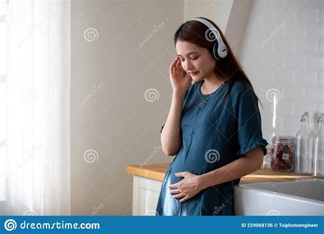 asian pregnant woman listening to music and singing and touching gently her tummy pregnancy
