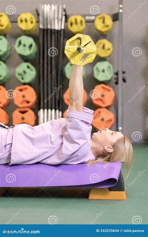 Woman Lying On Training Bench Lifting Barbell In Gym Pushing Exercise