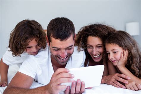 Familia Feliz Usando La Tableta Digital En Cama Foto De Archivo