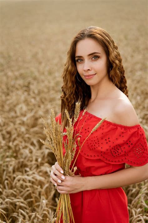 A Young Woman Holds Spikelets Against The Background Of A Wheat Field