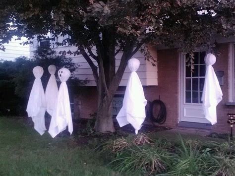 Three White Ghost Decorations Hanging From The Side Of A House In Front