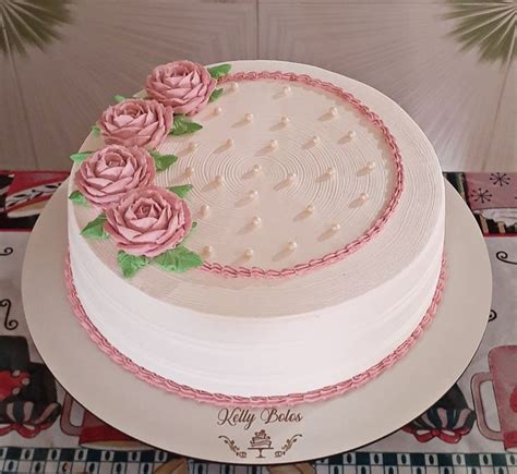 A White Cake With Pink Frosting And Roses On Top Is Sitting On A Table