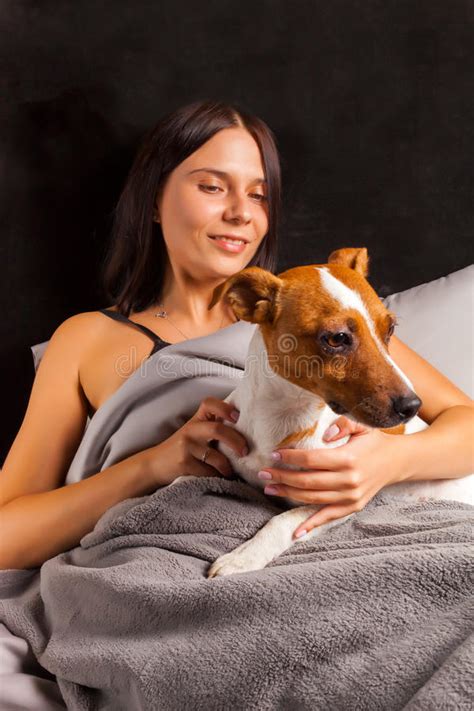 Young Beautiful Brunette Woman Plays In Bed With Her Dog Stock Image