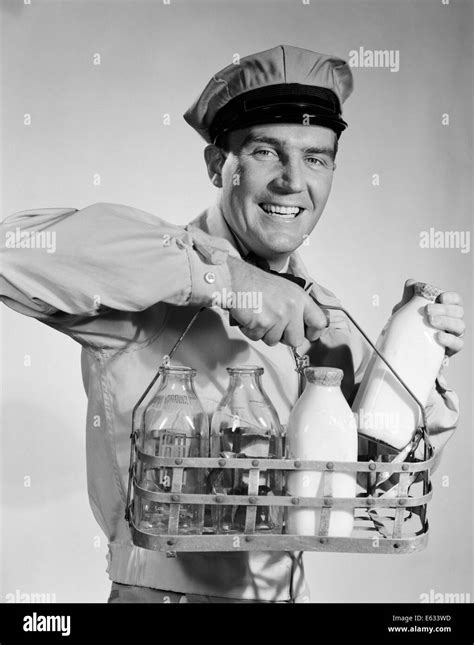 1950s 1960s Smiling Milkman In Uniform Looking At Camera Carrying Two