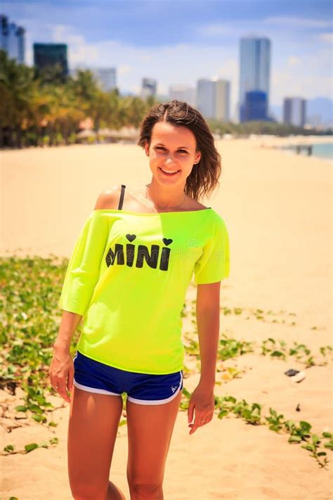 Slim Girl In Lemon T Shirt Smiles On Beach Against Resort City Stock