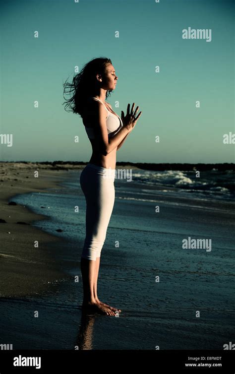Side View Of Woman Standing On Beach Doing Yoga With Hands In Prayer