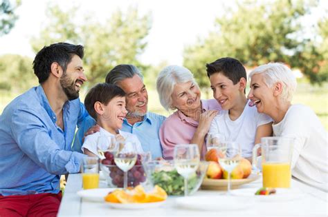 Familia Que Se Sienta En La Tabla Al Aire Libre Sonriendo Imagen De