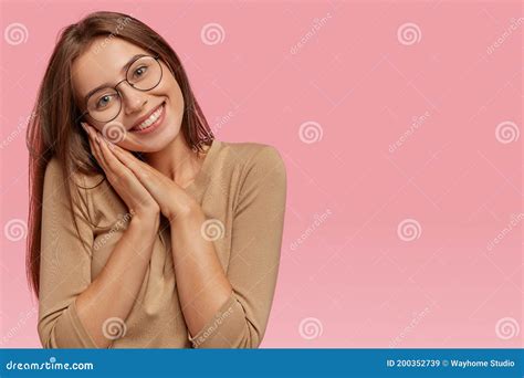 romantic happy good looking caucasian woman tilts head keeps both hands near cheek gazes with