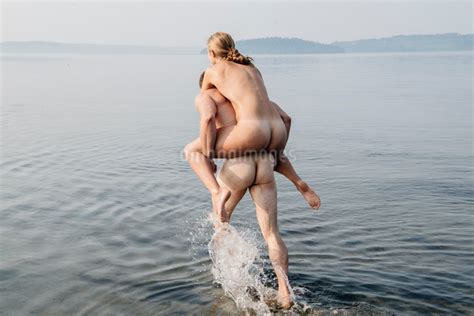 Nude man giving nude woman piggyback into waterの写真素材 FYI03599544