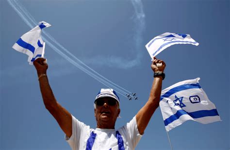 People watch as israeli air force planes fly in formation during an aerial show as part of the celebrations for israel's independence day marking the 73rd anniversary of the creation of the state. A man waves flags of Israel as Israeli Air Force planes ...