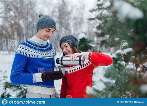 Young Couple Pouring Hot Tea Out Of Thermos In Winter Forest Happy