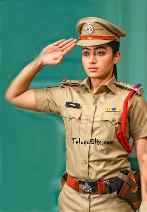 A Woman In Uniform Saluting With Her Hand On Her Head While Standing Next To A Green Wall