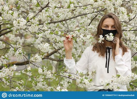 A Girl Allergic To Flowers In A Medical Mask Touches The Blossoming