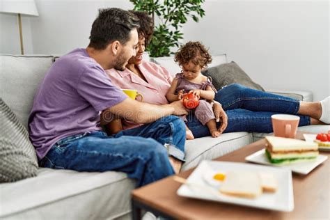 Couple And Daughter Having Breakfast Sitting On Sofa At Home Stock
