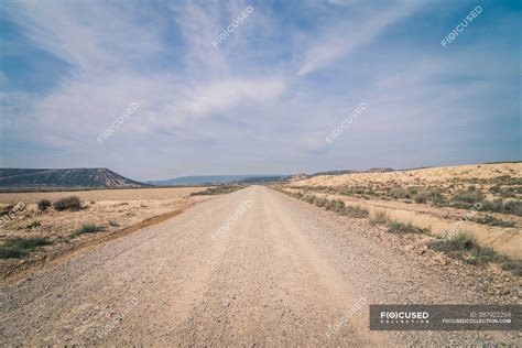 Desert Dusty Road Between Abandoned Dry Area With Vegetation In Semi
