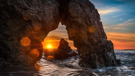 Download 1920x1080 Rocks Sunset Glare Ocean Arch Wallpapers For