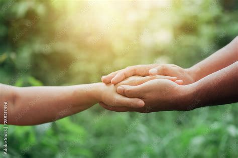 Close Up Of Two People Holding Hand Together Over Blurred Green Nature
