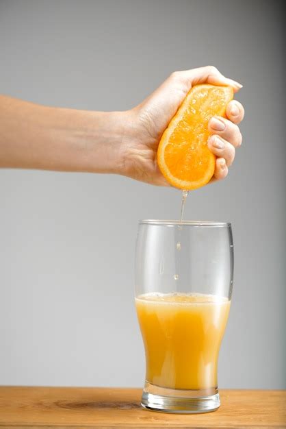 Mano Exprimiendo El Jugo De Naranja En Un Vaso Foto Gratis