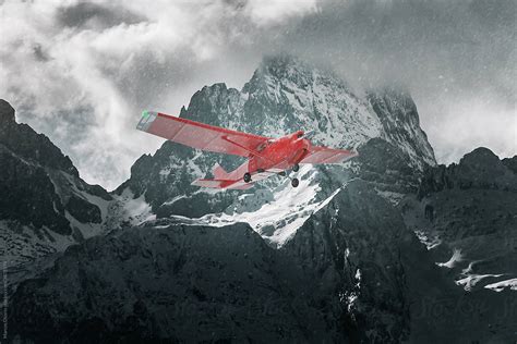 Red Plane Flying Over Snowy Mountains Del Colaborador De Stocksy