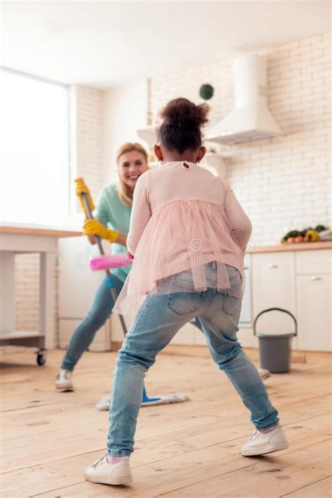 cute curly daughter mopping floor with mother and dancing stock image
