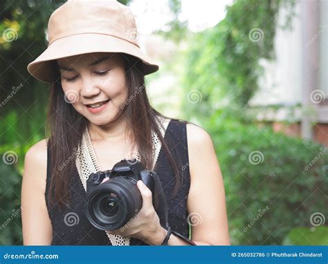 asian woman wearing hat and black top sleeveless standing in the garden and holding dslr