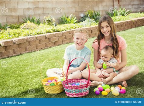 Three Cute Smiling Kids Collecting Eggs On An Easter Egg Hunt Outdoors
