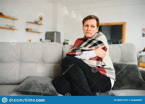 Middle Aged 50s Sick Frozen Woman Seated On Sofa In Living Room Covered