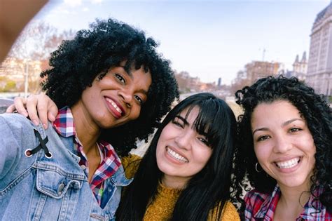 tres amigas jóvenes tomándose un selfie en la ciudad una haitiana negra y dos latinas foto